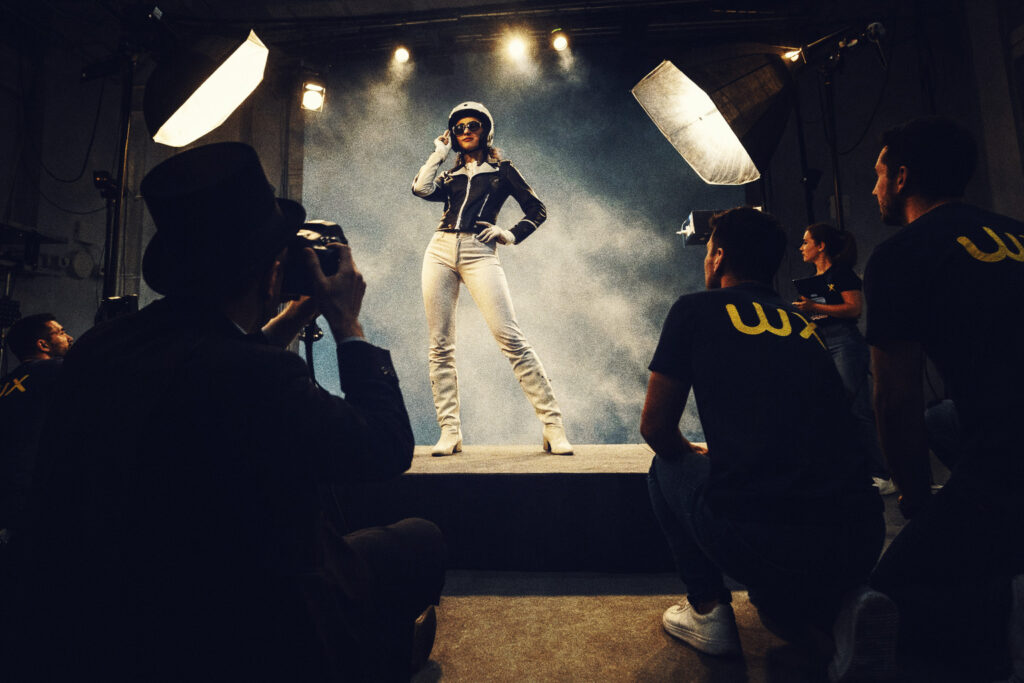 Illustration de la magie de l'IA pour la photogrpahie dans le ecommerce. Un modèle féminin est pris en photo par un photographe habillé en magicien, pendant que l'équipe Wexperience observe la prise de vue.